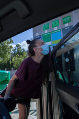 A young woman wearing a surgical mask putting petrol ,  in the oil station in times of the coronavirus pandemic