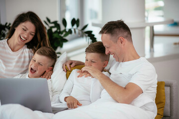 Obraz premium Young family watching movie on lap top. Beautiful parents with kids enjoying at home. 