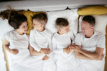 Young family enjoying in bed. Top view of happy parents with sons relaxing in bed.	