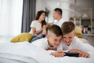 Two little brothers are playing games on the phone. Beautiful boys enjoying at home.