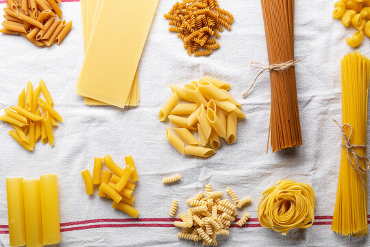 Variety of types and shapes of Italian pasta top view on white linen cloth