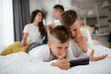 Two little brothers are playing games on the phone. Beautiful boys enjoying at home.