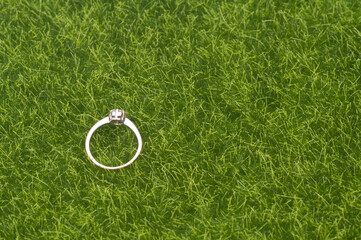 A single female wedding ring with diamond isolated over green grass