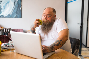 Bald bearded man in white tshirt holding an apple and reading something exciting