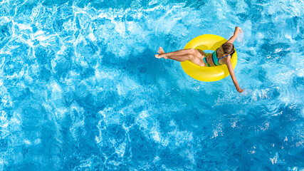 Active young girl in swimming pool aerial top view from above, child relaxes and swims on inflatable ring donut and has fun in water on family vacation, tropical holiday resort
