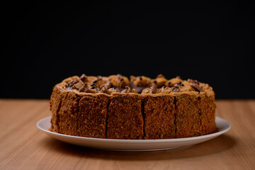 Delicious nut cake glazed with dark chocolate icing served on a white plate on light wooden table background.