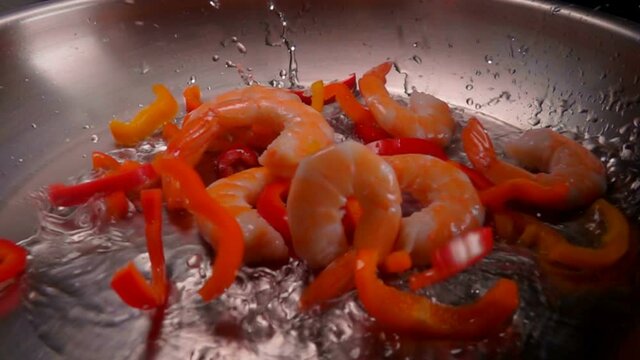 Close-up of large shrimps and red pepper falling in a hot oil with splashes on the pan. Shrimp Recipe