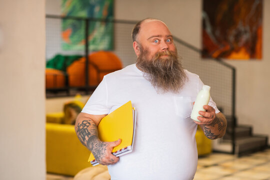 Bald bearded plump manstanding and holding a bottle with milk
