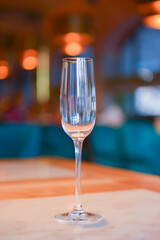 Transparent empty champagne glass on the rustic wooden table over blurred restaurant background.