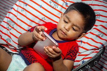 Before going to sleep a child is lying a homemade hammock and watching cartoons using a smartphone. Kids playing with smartphone. Mobile phone and internet addiction concept.