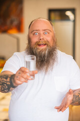Bald bearded plump man holding a glass with water