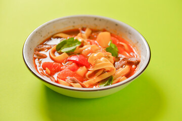 Bowl of minestrone pasta soup, served in a white bowl over bright green background. Copy space design banner.