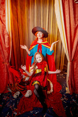 Family during a stylized theatrical circus photo shoot in a beautiful red location. Models grandmother and granddaughter posing on stage with curtain