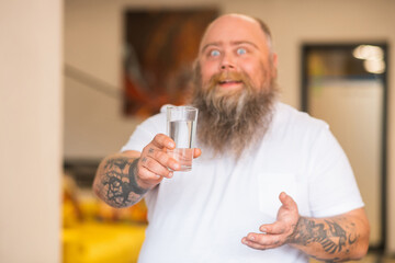 Bald bearded plump man holding a glass of water in his hand