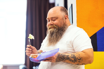 Bald bearded plump man holding a lunchbox in his hand