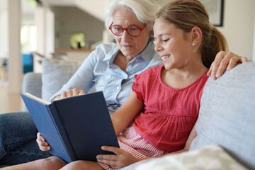 Grandmother with grandkid reading book in sofa