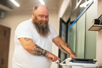 Bald bearded abdominous man making copy on xerox