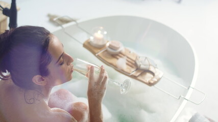 Romantic woman drinking champagne in luxury bath. Sexy girl relaxing in bathtub.