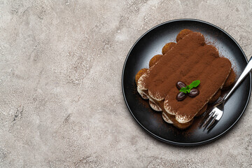 Classic tiramisu dessert on ceramic plate on light grey concrete background