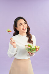 Portrait of a happy playful girl eating fresh salad from a bowl over purple background