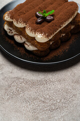 Classic tiramisu dessert on ceramic plate on light grey concrete background