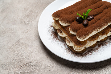 Classic tiramisu dessert on ceramic plate on light grey concrete background