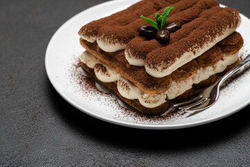 Classic tiramisu dessert on ceramic plate on dark concrete background