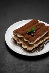 Classic tiramisu dessert on ceramic plate on dark concrete background