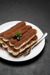 Classic tiramisu dessert on ceramic plate on dark concrete background