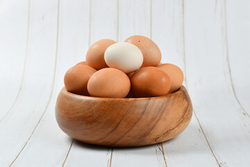Full wooden plate of brown chicken eggs and one white
