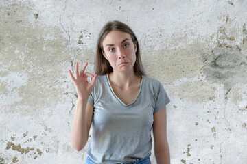 Woman showing ok sign with fingers digusted on a gray concrete background