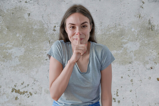 Young beautiful woman keeping finger on her lips and asking to keep quiet