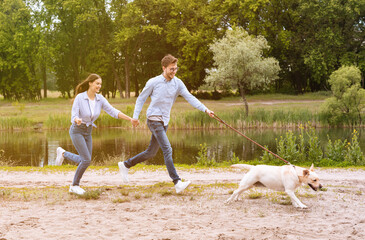 Excited couple and retriever running near lake
