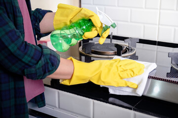 Woman cleaning surface kitchen furniture. Hand in yellow rubber glove wiping surfaces disinfection spray bottle surfaces and wipes.