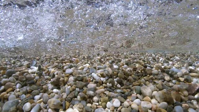 Pebbles rocks underwater below water surface with small waves breaking on the shore, Mediterranean sea, France