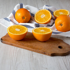 Halved and whole oranges on a white wooden background, side view.