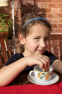 Ritratto di una bambina chiara che fa merenda con il tè e i biscotti nel terrazzo di casa