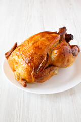 Homemade tasty rotisserie chicken on white plate over white wooden surface, low angle view. Close-up.