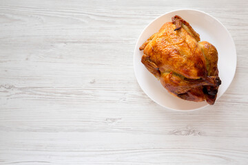 Homemade traditional rotisserie chicken on a white plate on a white wooden background, top view. Flat lay, overhead, from above. Copy space.