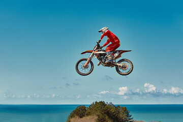 Fototapeta premium Extreme concept, challenge yourself. Extreme jump on a motorcycle on a background of blue sky with clouds. Copy space, all or nothing.