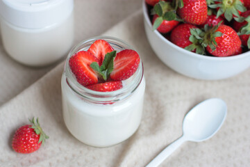A glass jar of home made yoghurt decorated with strawberries and mint on natural color fabric.