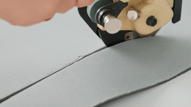 Female worker on a sewing manufacture uses electric cutting fabric machine. Sewing production line
