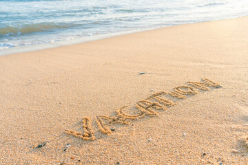 Vacation word handwritten on sandy beach natural outdoors background.
