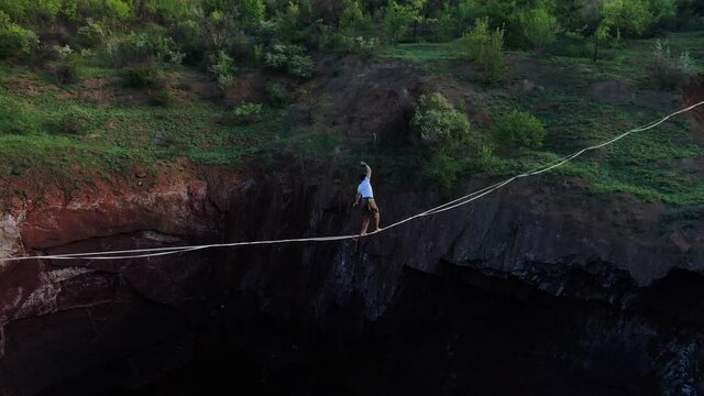 Aerial footage of a man walking on a tightrope, dark abyss is under him, 4k