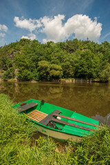 small green boat at the shore of river with trees on other side