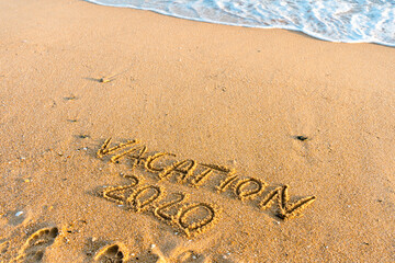 2020 Vacation handwritten on sandy beach natural outdoors background.