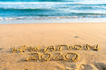 2020 Vacation handwritten on sandy beach natural outdoors background.