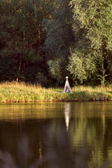 Fototapeta premium Pond on a sunny day. Wigwam on the other shore. Lake in the forest. Green fairy tale. High quality photo