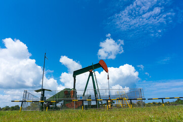 Fototapeta na wymiar Oil pump jack in work. Oil industry in Seria, Brunei Darussalam on a sunny day with cloudy blue skies.