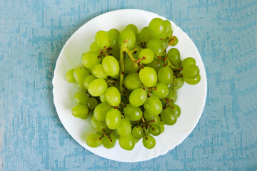 Grona from white grapes without seeds in a white plate on a blue textural background top view . raw...